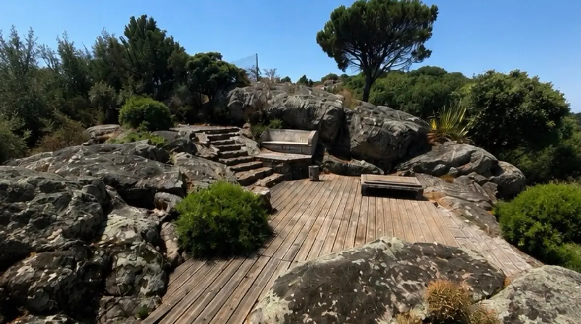 Avant travaux : l'ancienne terrasse en bois grisé entre les rochers, au pied d'un escalier en pierre