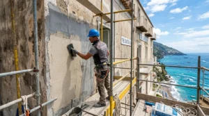Ouvrier rénovant une façade côtière avec matériaux résistants, sous un ciel marin lumineux.